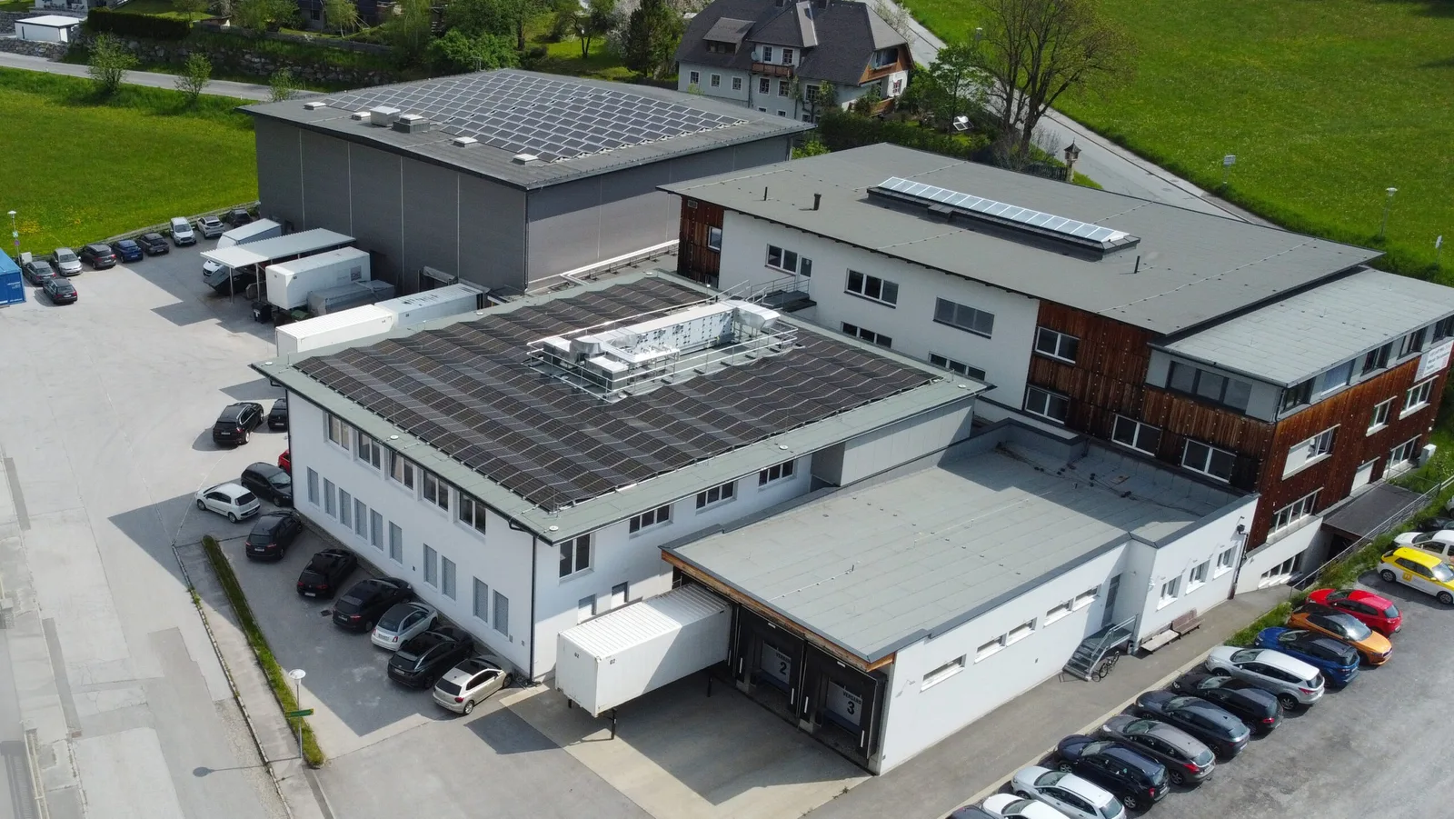 Luftbild des Firmengebäudes in Tamsweg mit Photovoltaik auf dem Dach, Parkplätzen und Wiesen ringsum